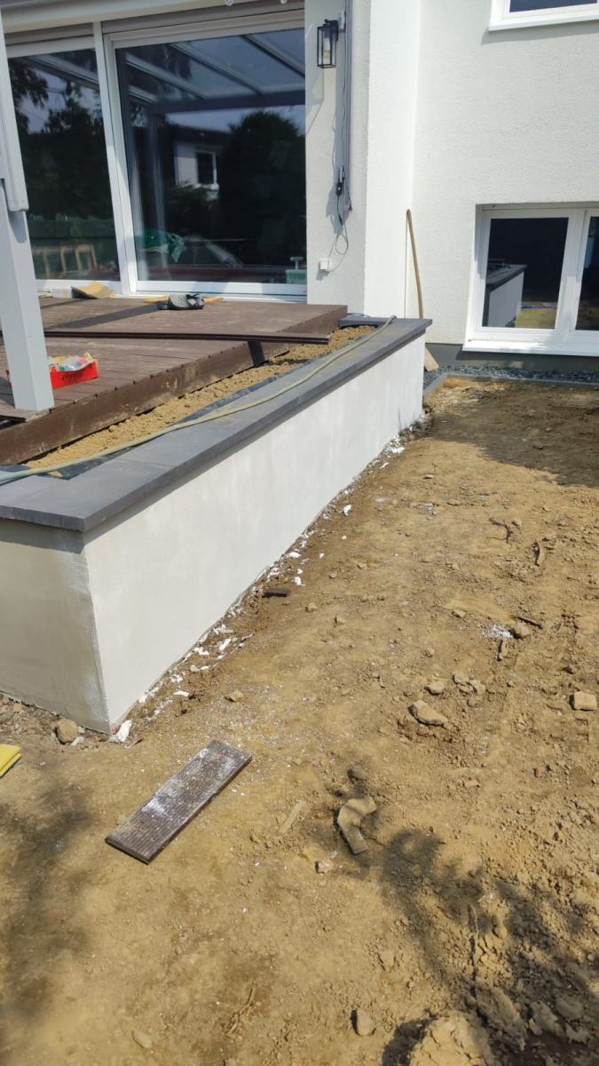 Terrassenkante mit Abdeckplatte und verputztem Sockel vor dem Rasenaufbau