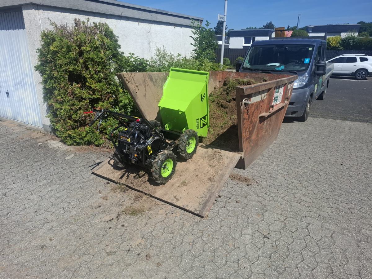 Minidumper entlädt Aushub in einen Container vor dem Haus